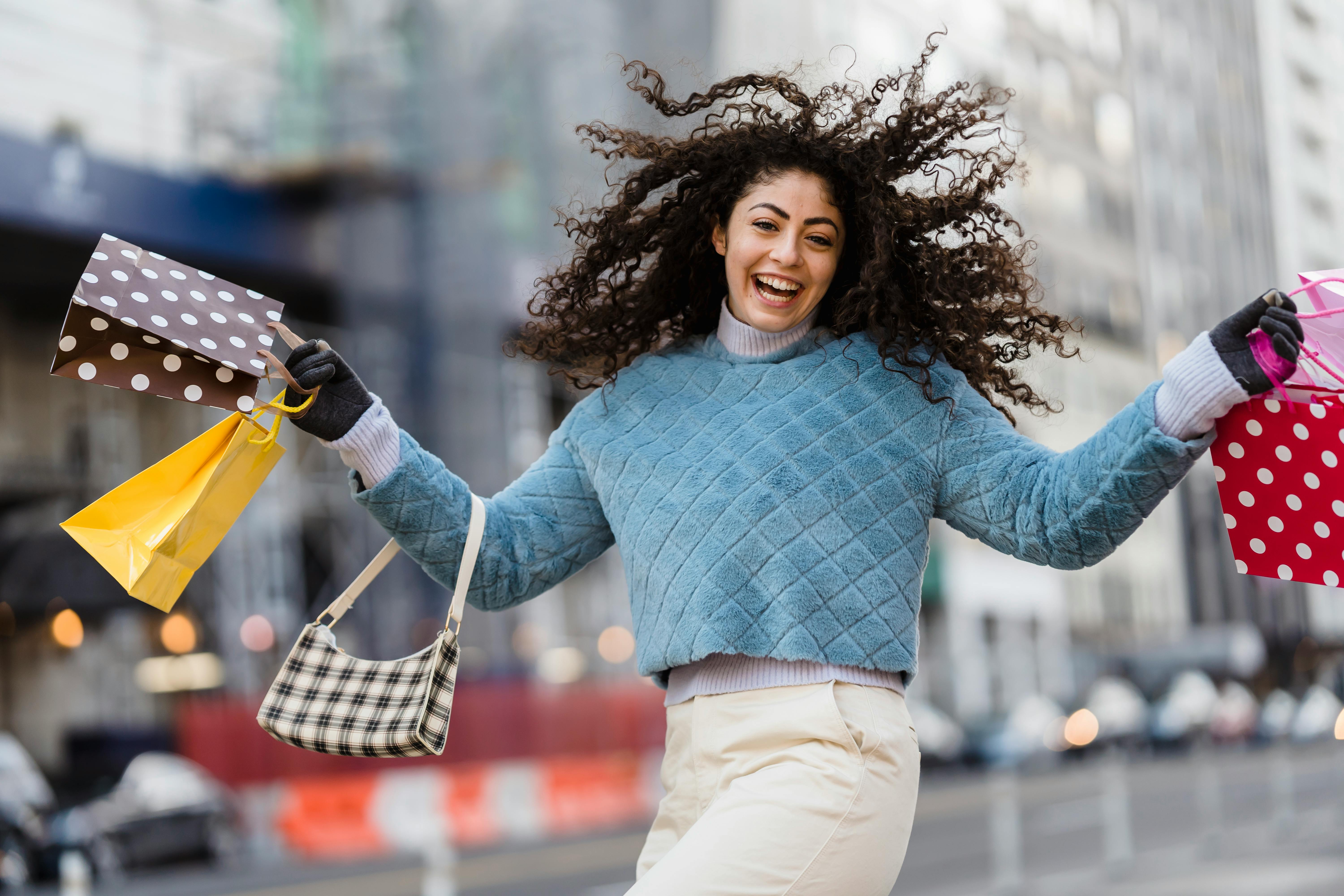 Cheerful woman enjoying a shopping spree outdoors in a city setting, showcasing vibrant lifestyle.